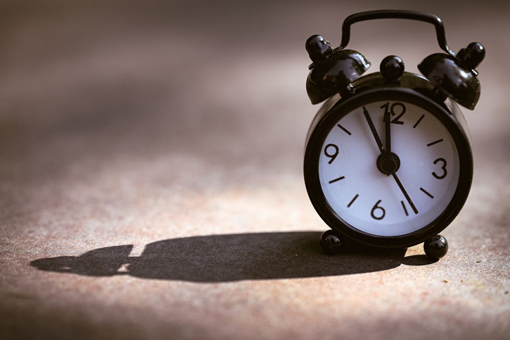A classic black alarm clock showing five minutes to twelve on a textured surface with dramatic shadow for the post "What Time of Day Does the Canada Child Benefit Drop Into Your Bank Account?"
