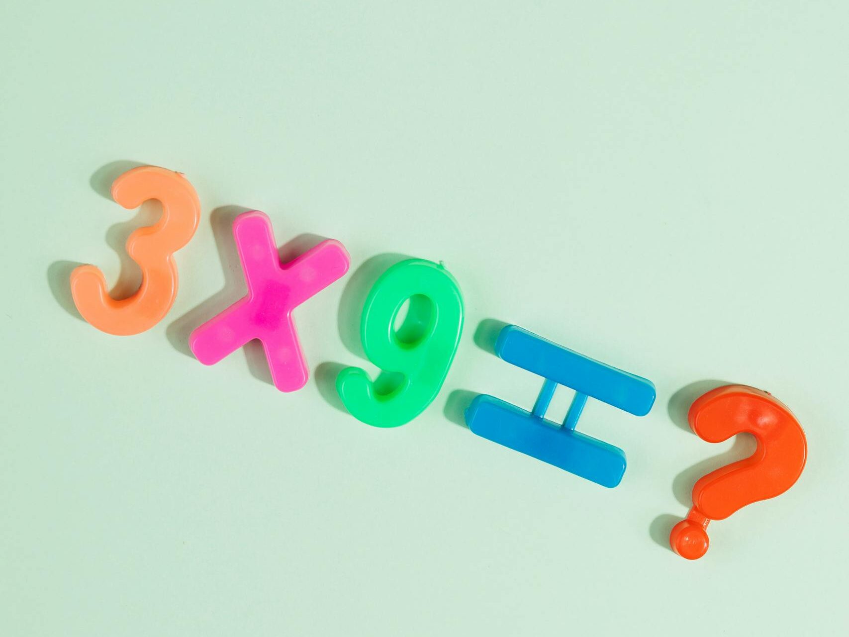 Bright numbers and symbols for multiplication equation on pastel green surface.